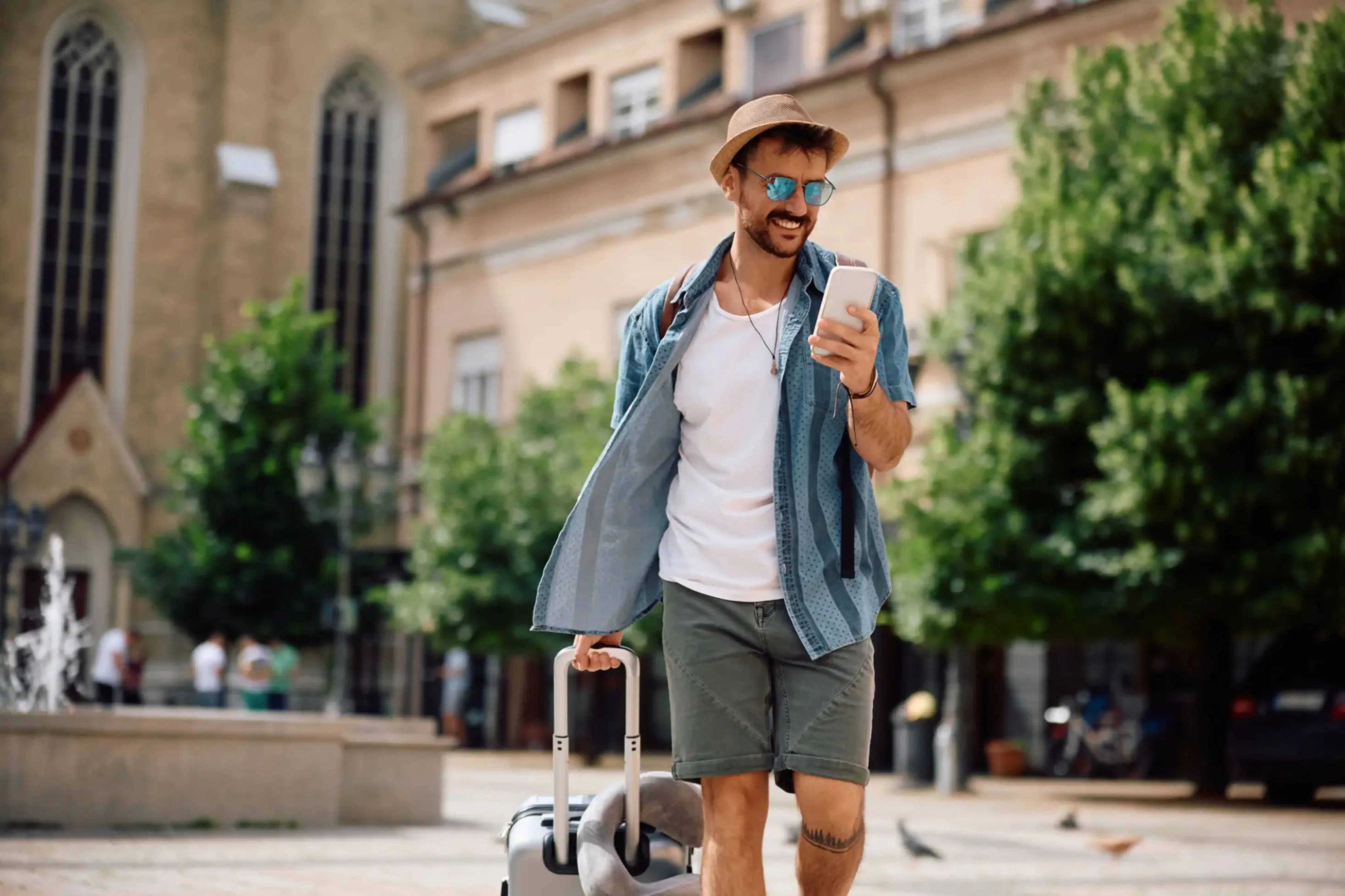 "Young male tourist with suitcase exploring city using smartphone"