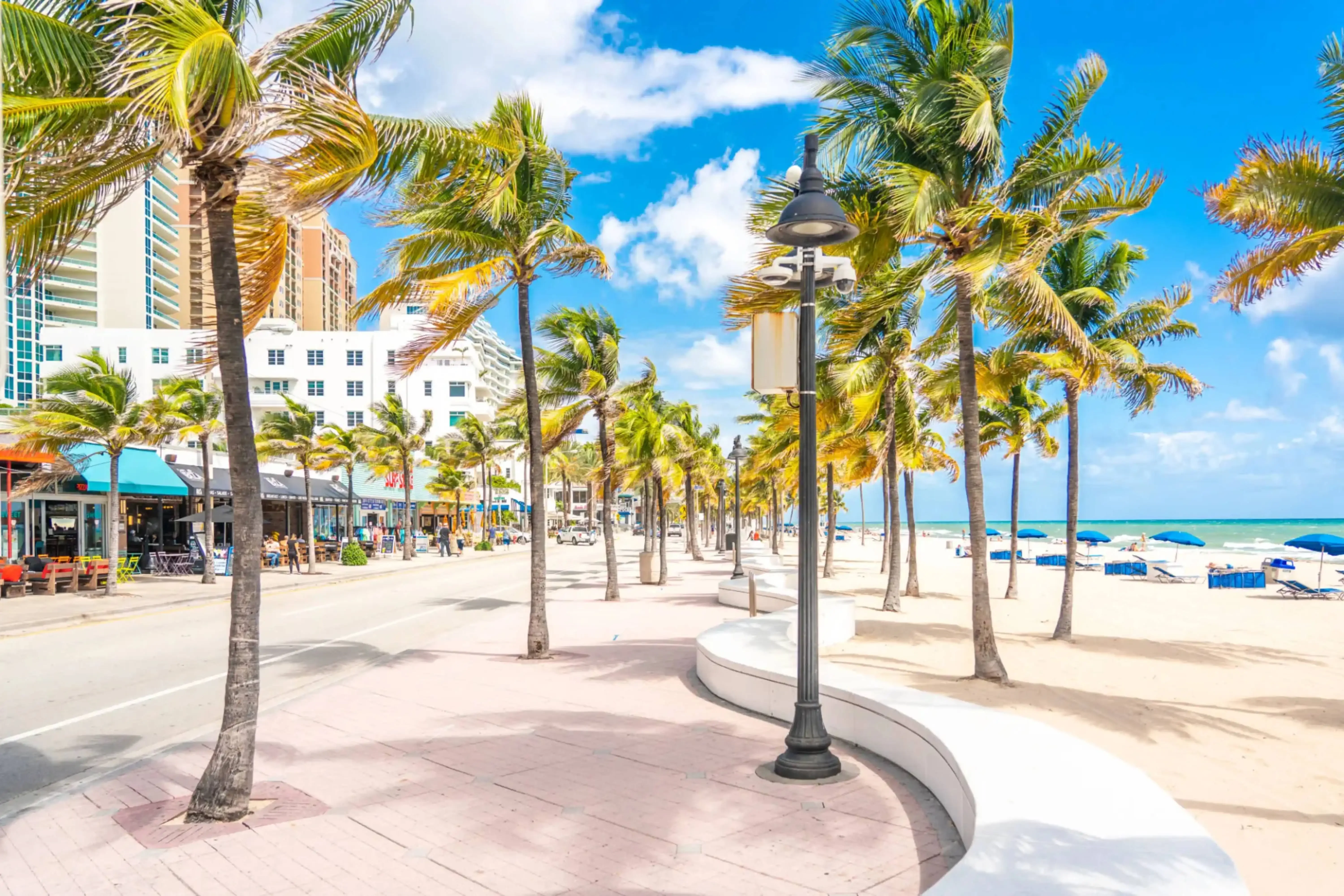 "Palm-lined oceanfront promenade with beach and resorts in tropical city"