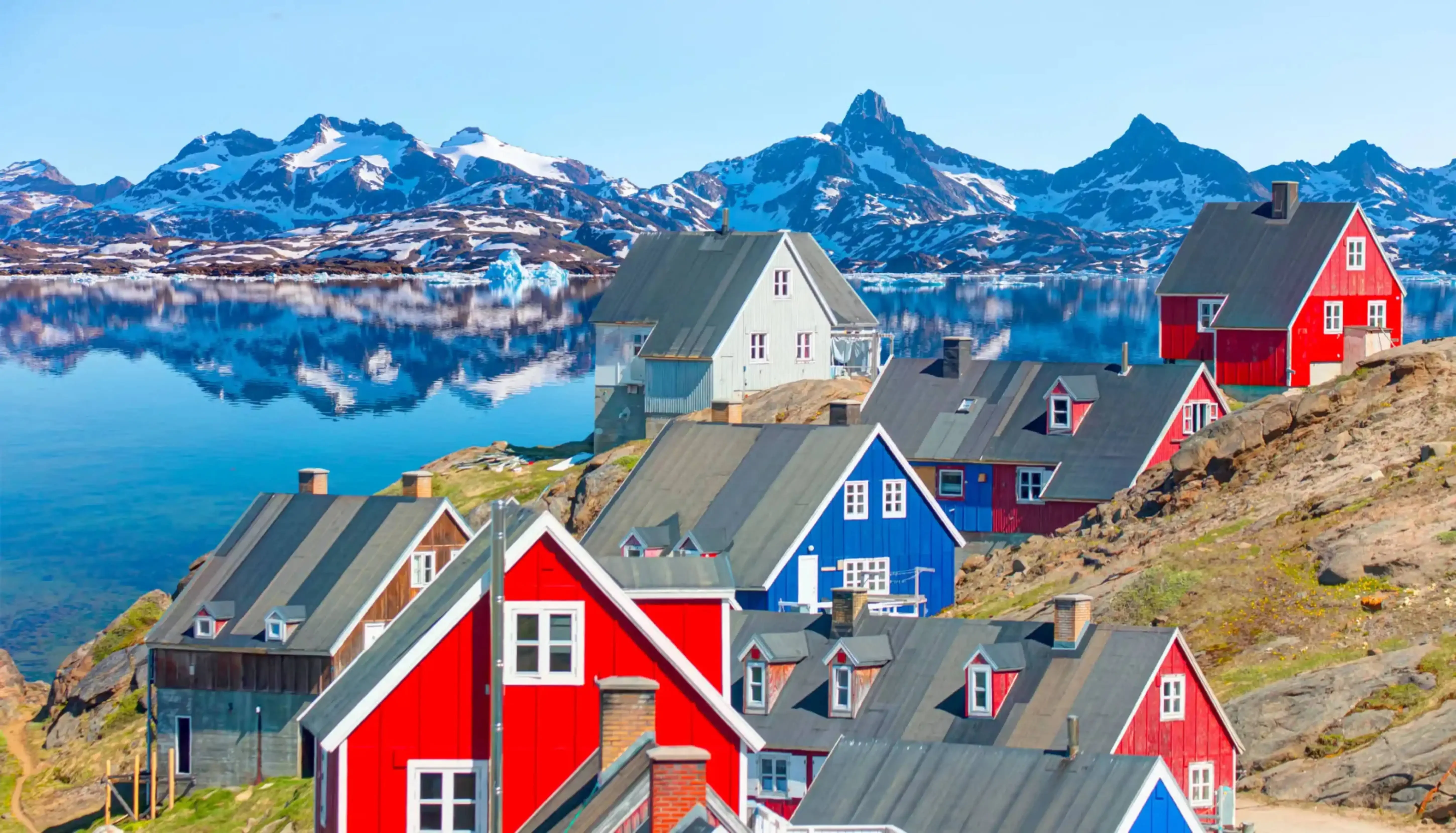 "Colorful houses in Greenland with fjord and snow-capped mountains in background"