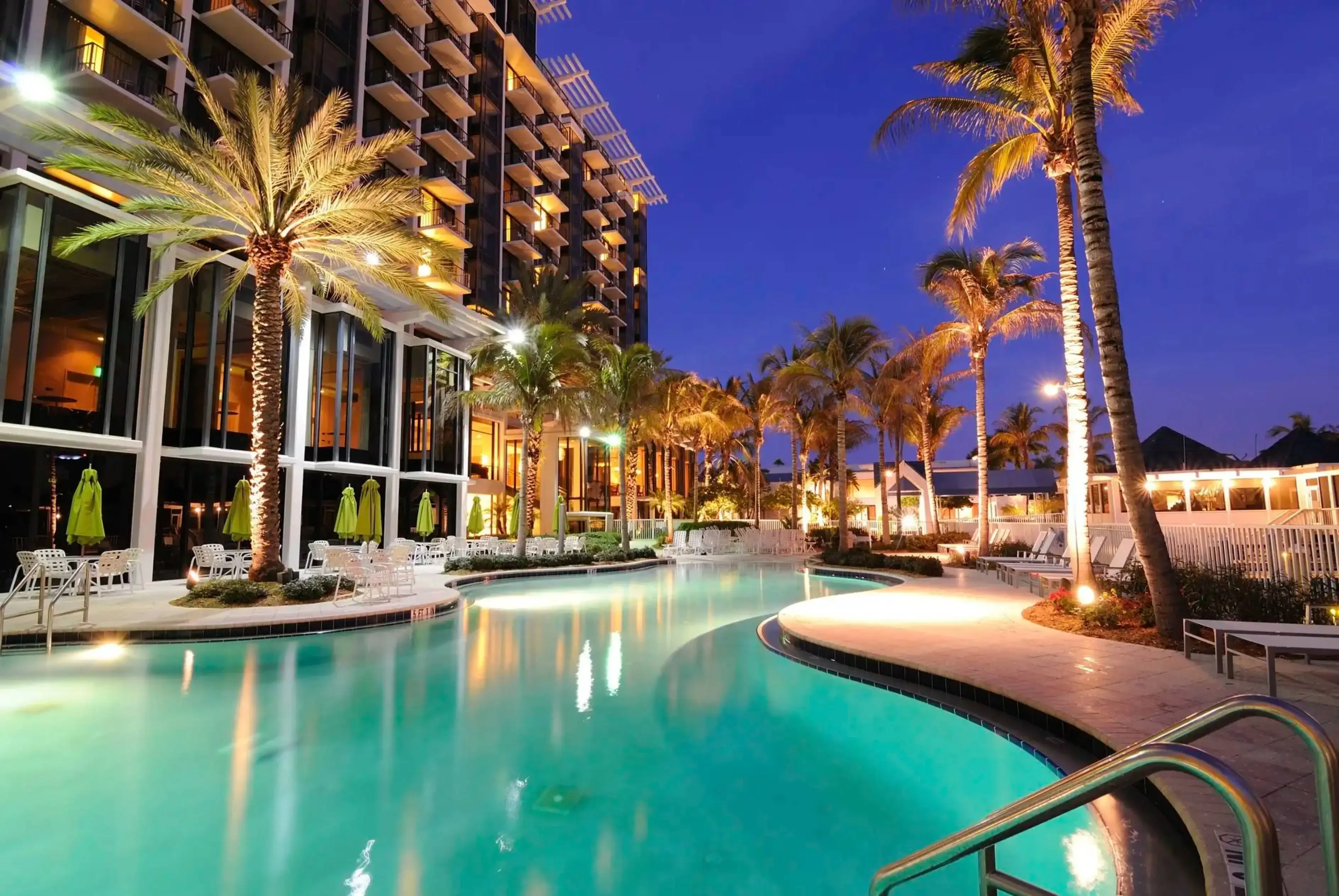 "Luxury resort poolside at night with palm trees and illuminated hotel buildings"