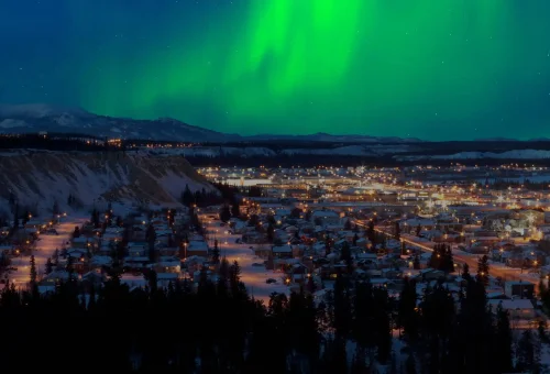 "Vibrant Northern Lights glowing above a snowy townscape at night in the Arctic Circle"