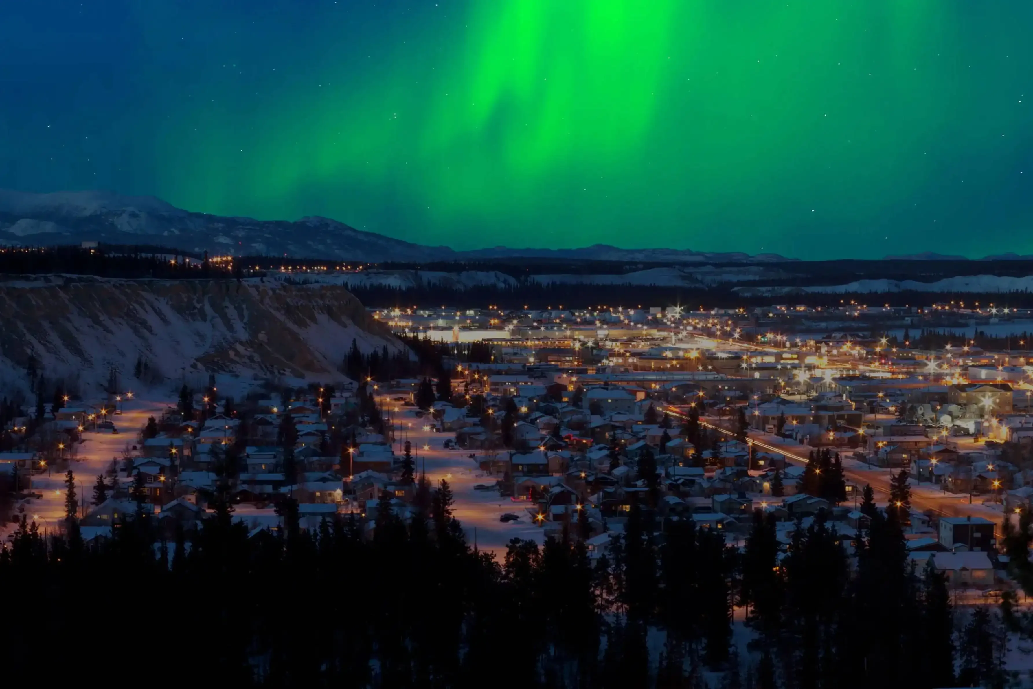 "Vibrant Northern Lights glowing above a snowy townscape at night in the Arctic Circle"