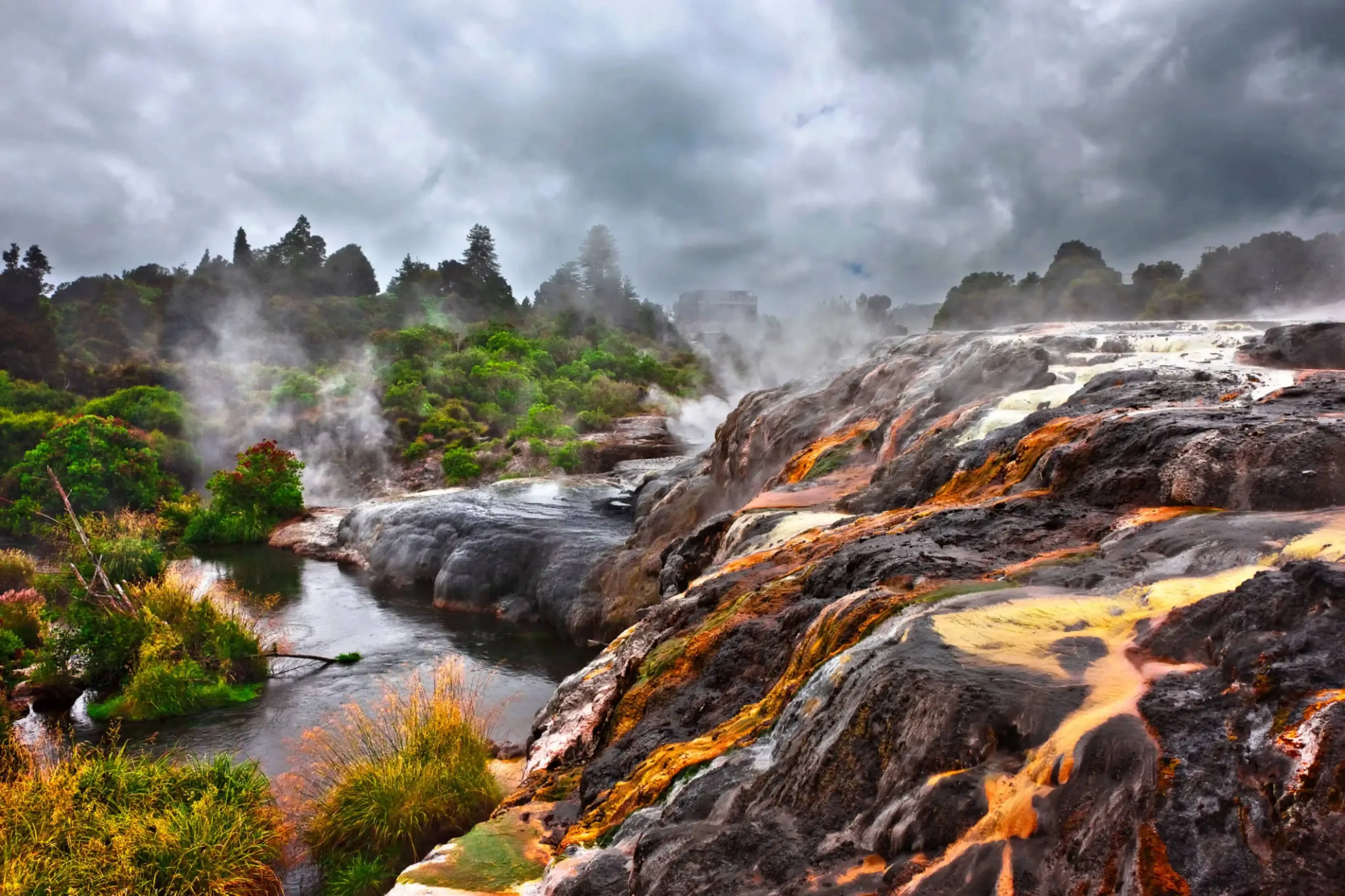 "Steaming volcanic terrain with flowing lava and lush greenery under cloudy sky"