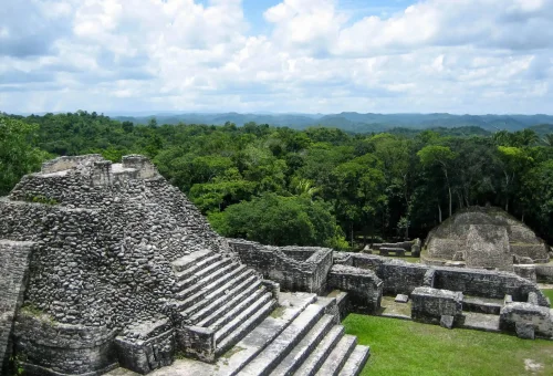 "Ancient stone pyramid ruins surrounded by lush green jungle under a partly cloudy sky"