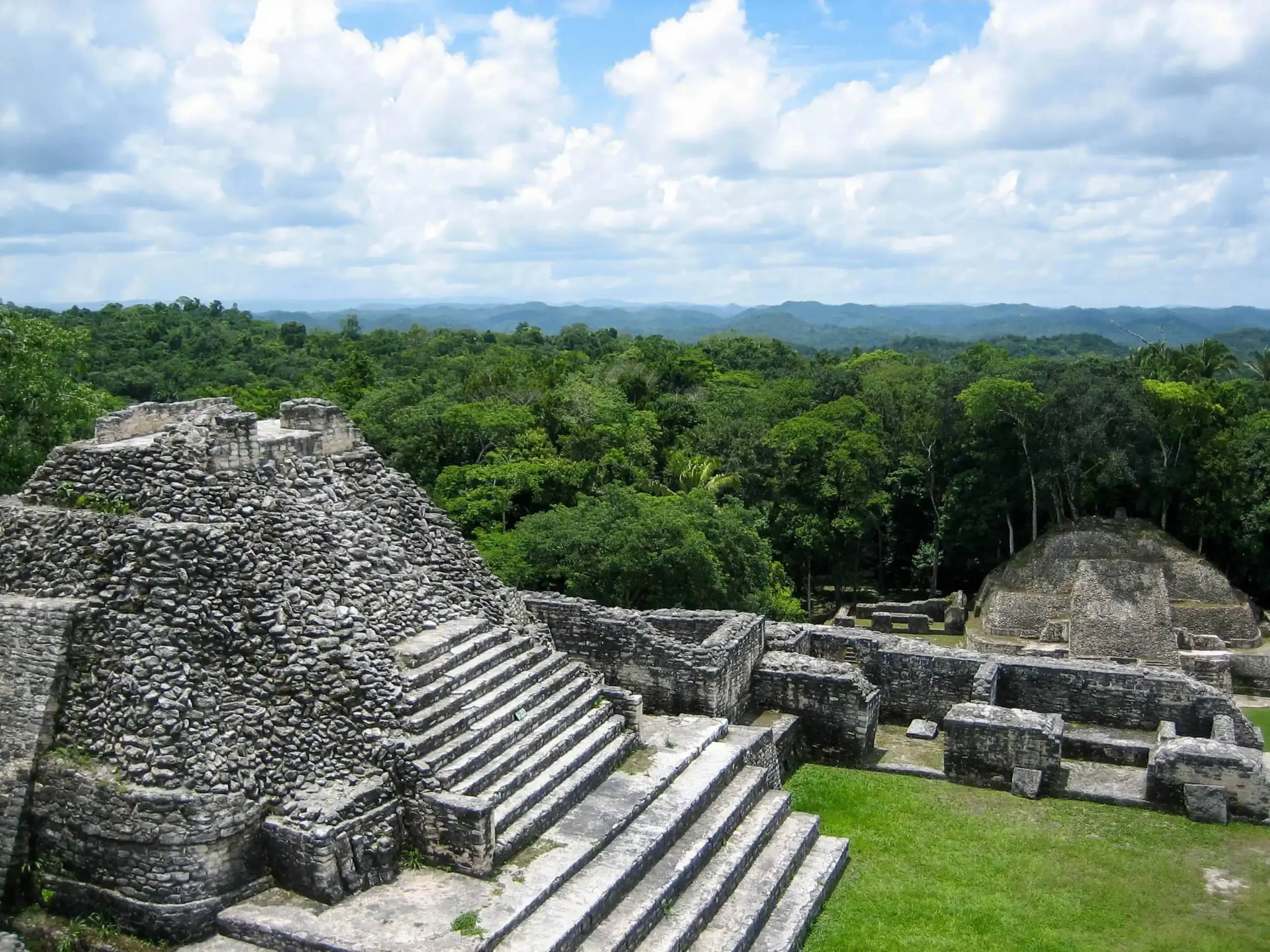 "Ancient stone pyramid ruins surrounded by lush green jungle under a partly cloudy sky"