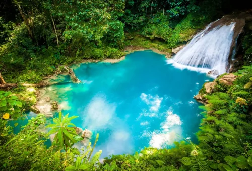 "Reach Falls waterfall flowing into a turquoise pool surrounded by dense tropical forest in Portland Parish, Jamaica."