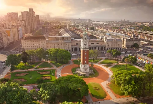 "Aerial view of Torre Monumental clock tower in Plaza Fuerza Aérea Argentina, with Retiro train station and Buenos Aires skyline in the background."
