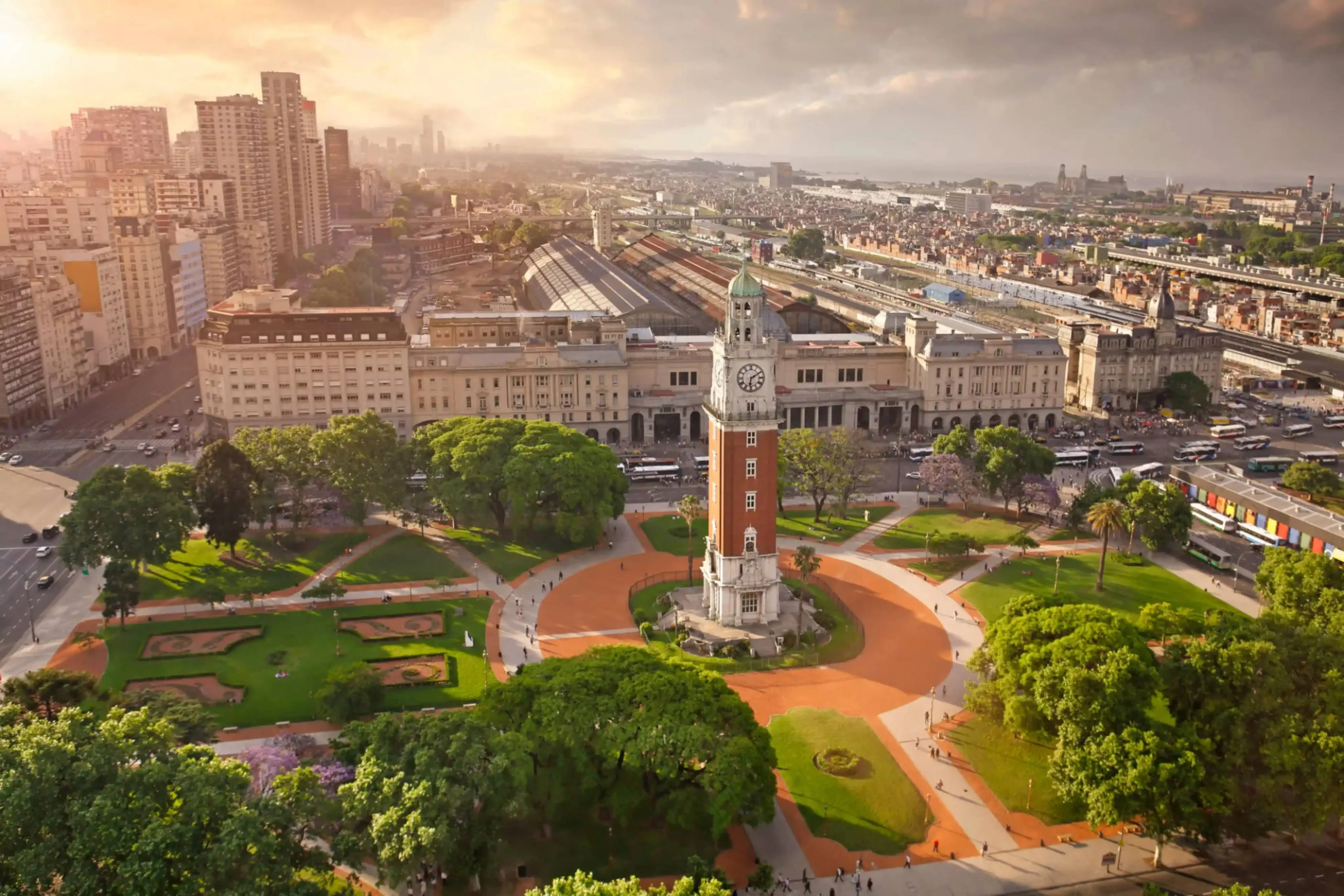 "Aerial view of Torre Monumental clock tower in Plaza Fuerza Aérea Argentina, with Retiro train station and Buenos Aires skyline in the background."