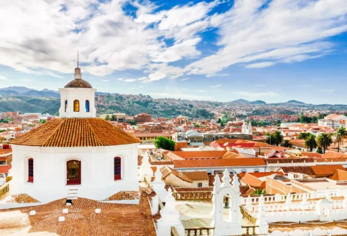 "Scenic rooftop view of colonial Sucre, Bolivia, featuring the white dome of La Merced Church and terracotta rooftops under a partly cloudy sky."