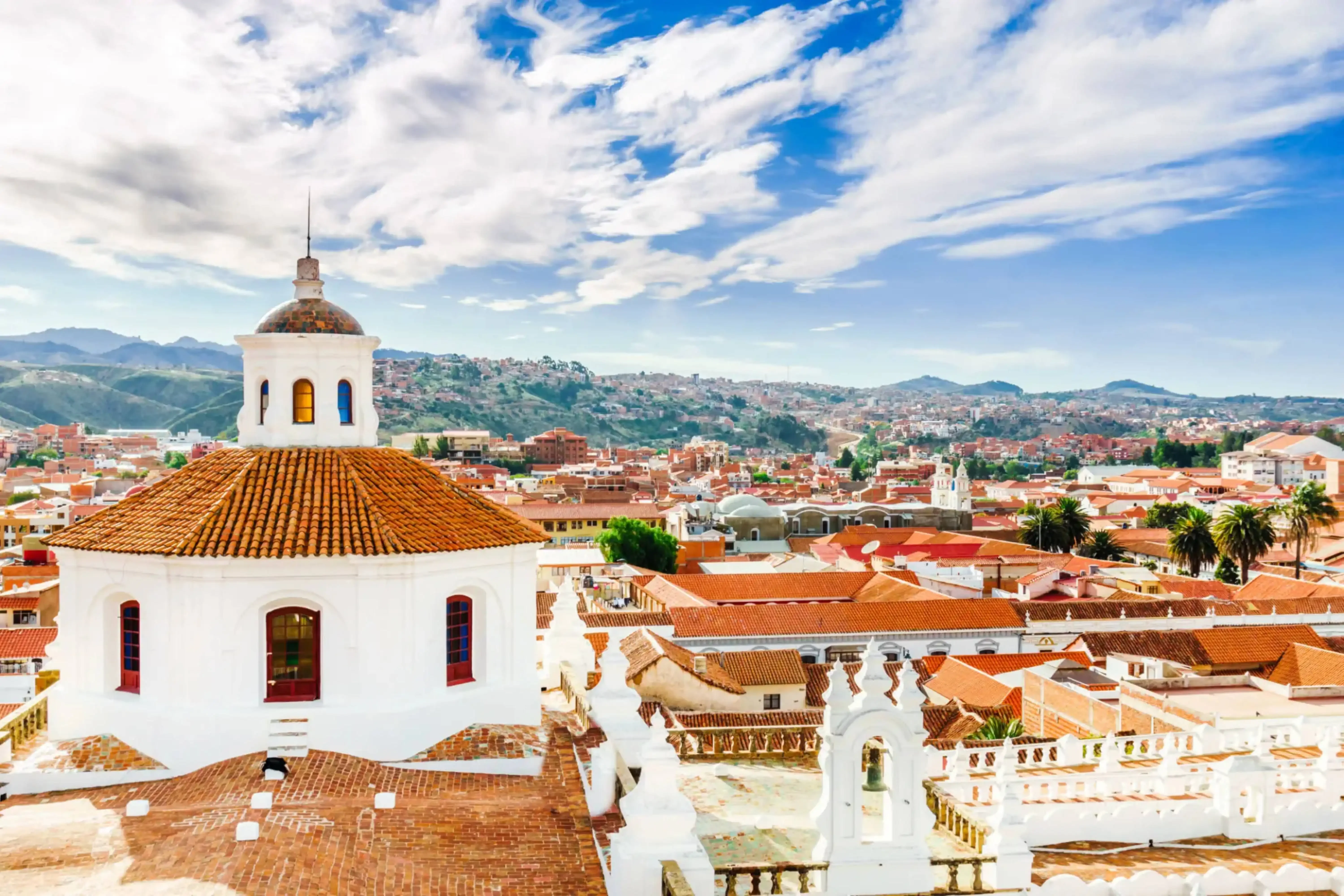 "Scenic rooftop view of colonial Sucre, Bolivia, featuring the white dome of La Merced Church and terracotta rooftops under a partly cloudy sky."