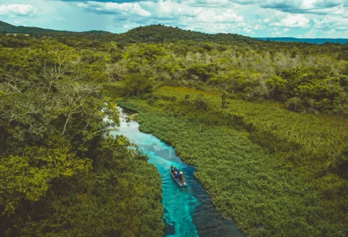 "Overhead view of a canoe on a narrow turquoise river winding through lush jungle vegetation in the Mountain Pine Ridge Forest Reserve, Belize."