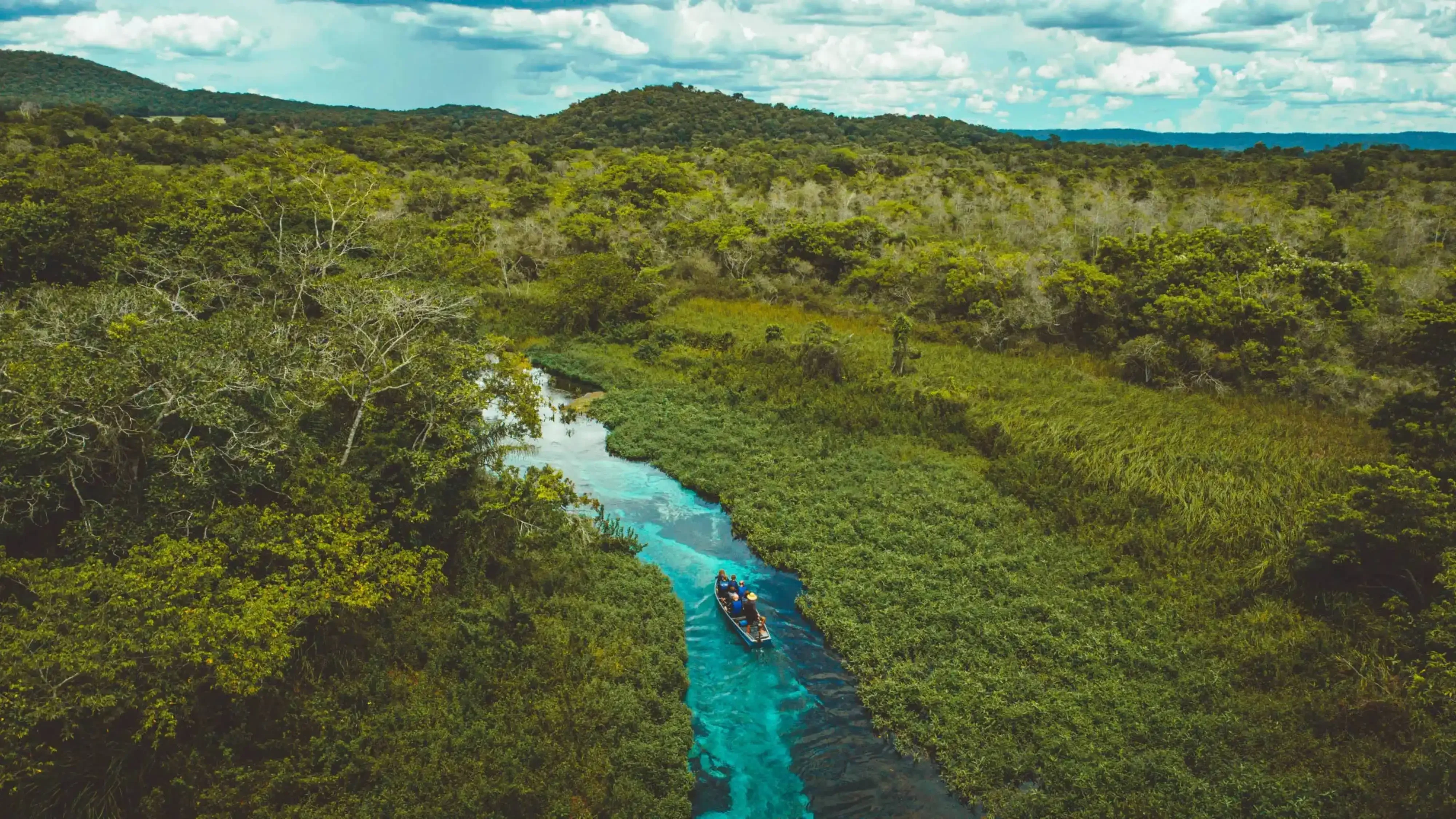 "Overhead view of a canoe on a narrow turquoise river winding through lush jungle vegetation in the Mountain Pine Ridge Forest Reserve, Belize."