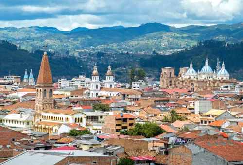 "Panoramic view of Cuenca city in Ecuador with colonial buildings, churches, and surrounding mountains."
