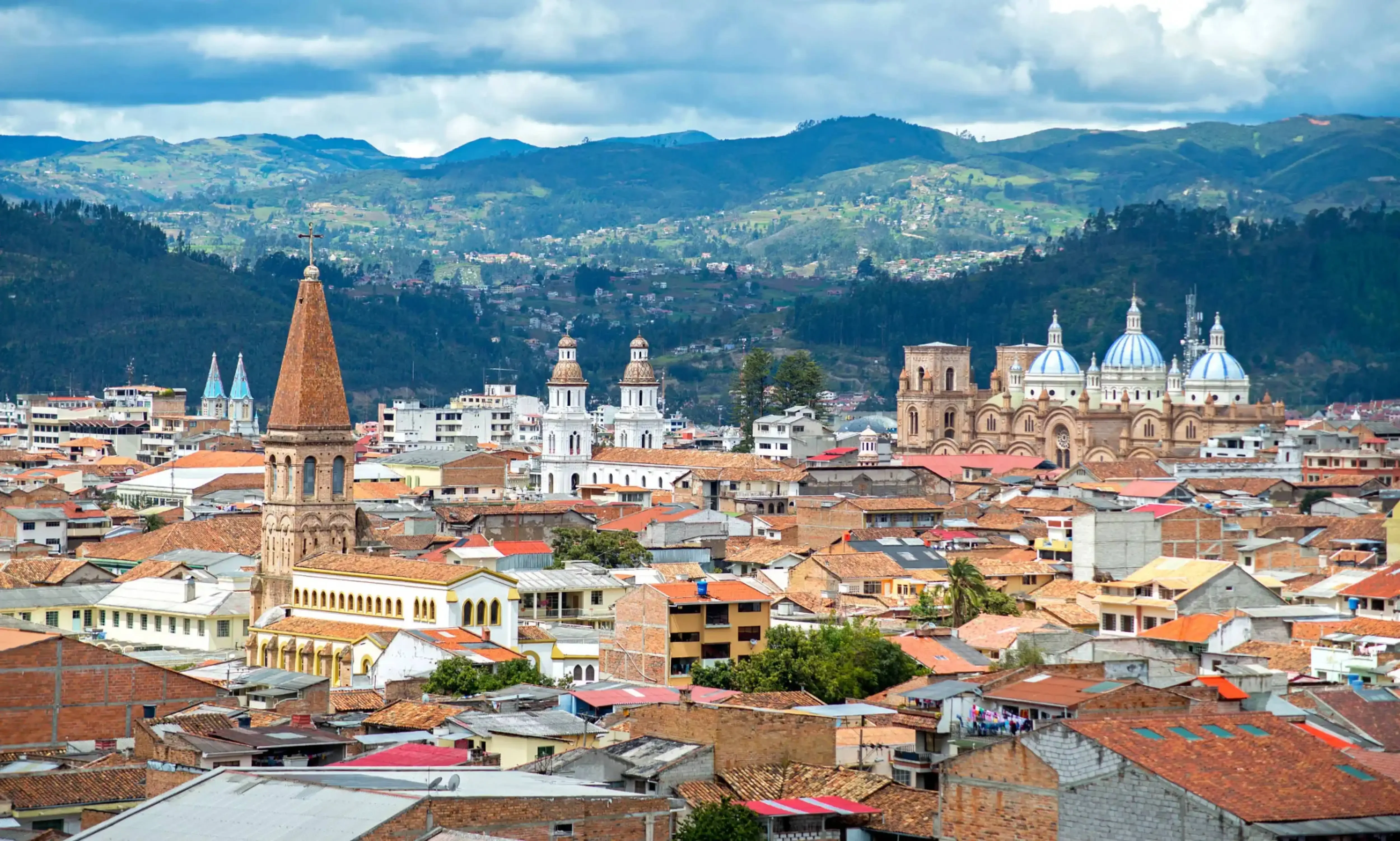 "Panoramic view of Cuenca city in Ecuador with colonial buildings, churches, and surrounding mountains."