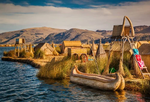 "Traditional reed boats and homes on the Uros Floating Islands, Lake Titicaca, on the Peru-Bolivia border, with mountains in the background."