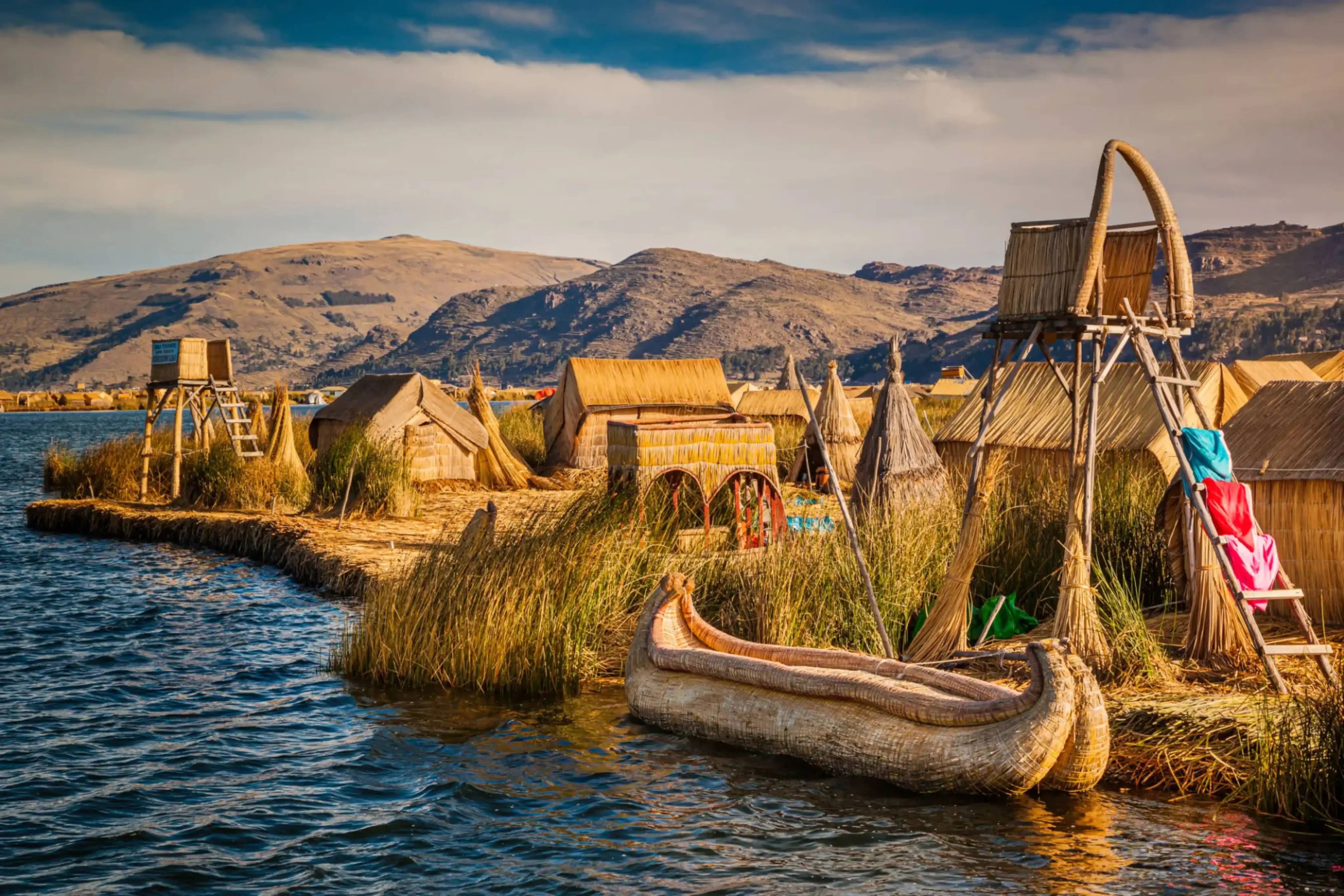 "Traditional reed boats and homes on the Uros Floating Islands, Lake Titicaca, on the Peru-Bolivia border, with mountains in the background."