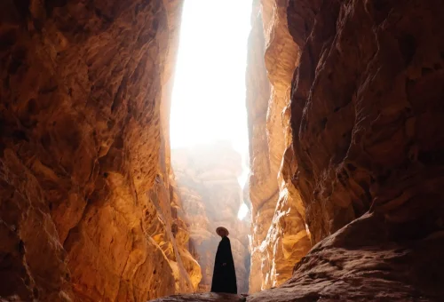 "Silhouette of a person standing in Al Siq, the narrow sandstone gorge leading to Petra, Jordan, with sunlight illuminating the canyon walls."