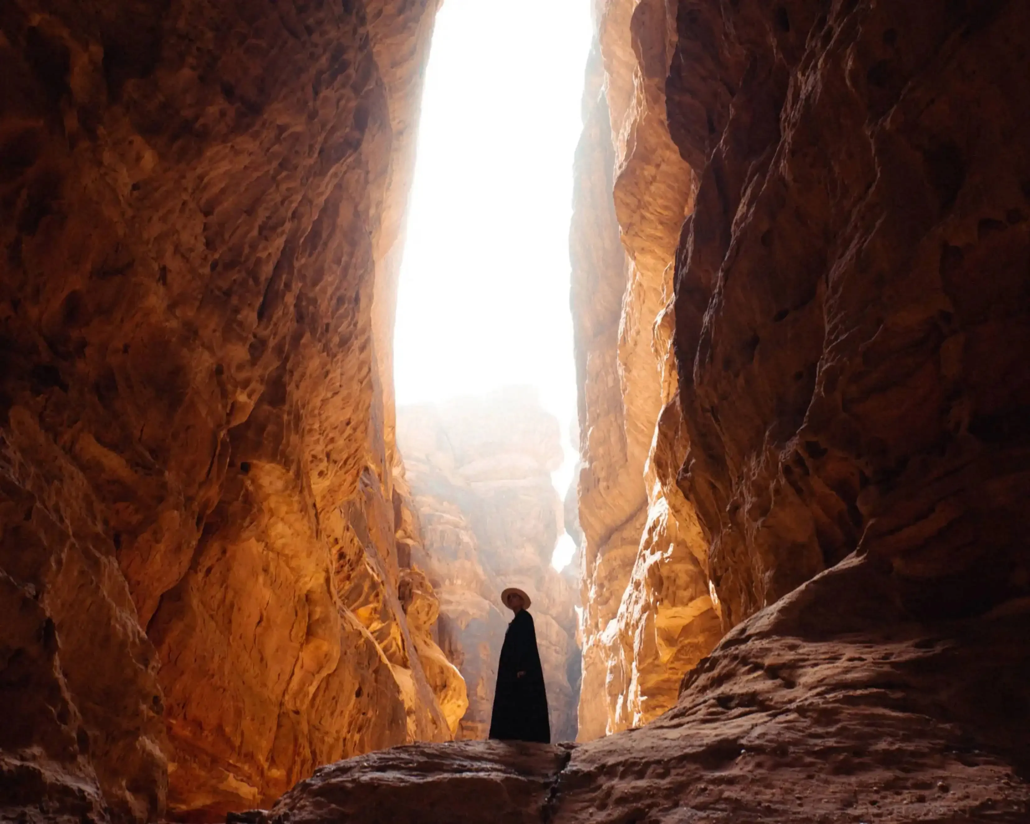 "Silhouette of a person standing in Al Siq, the narrow sandstone gorge leading to Petra, Jordan, with sunlight illuminating the canyon walls."