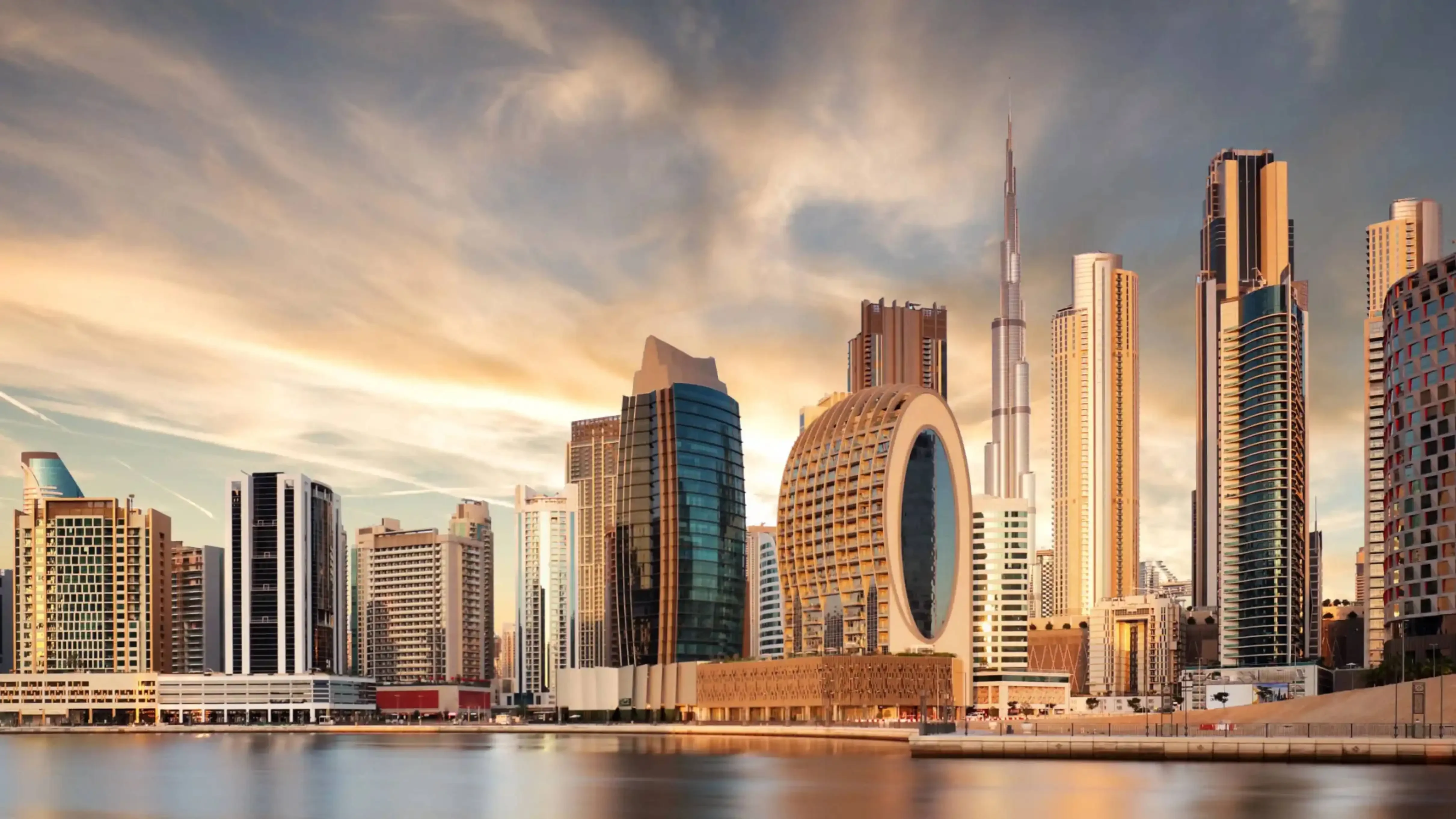 "Modern skyline of Dubai, UAE featuring the Burj Khalifa and circular waterfront skyscrapers during a golden sunset."