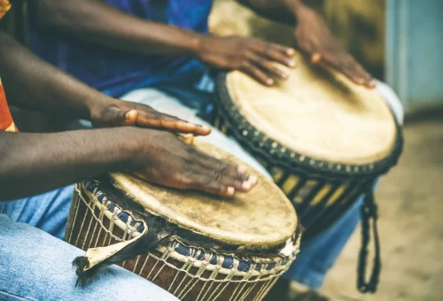 "Close-up of hands playing traditional African djembe drums during a cultural performance in West Africa."