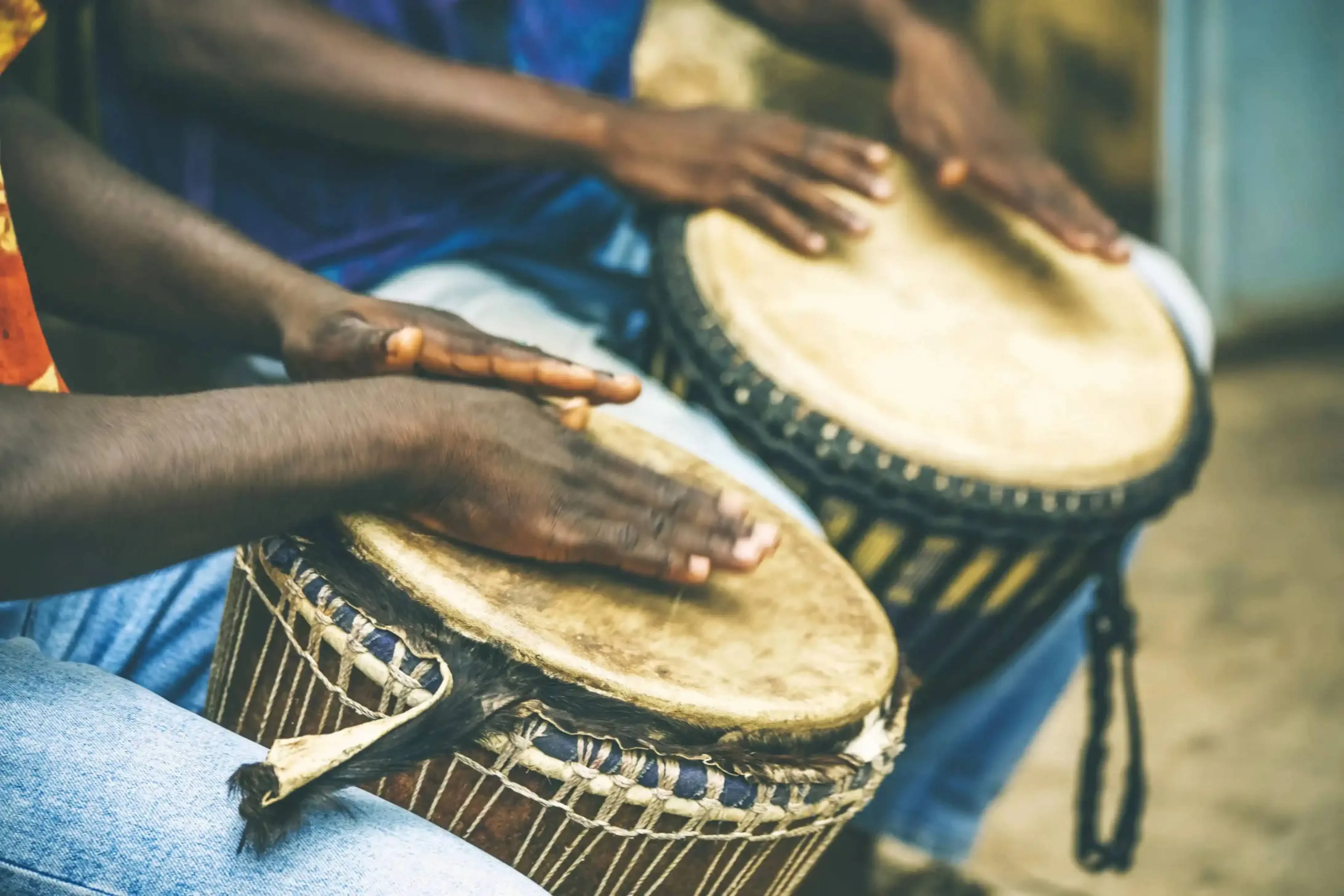 "Close-up of hands playing traditional African djembe drums during a cultural performance in West Africa."
