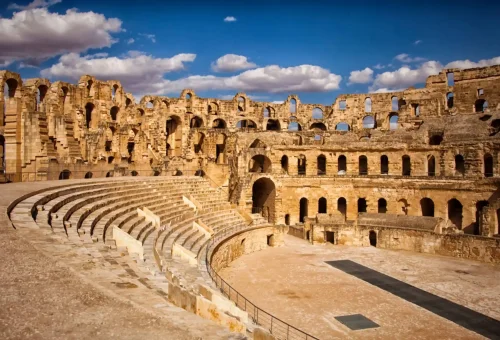 "Ancient Roman amphitheater ruins under a blue sky with scattered clouds."