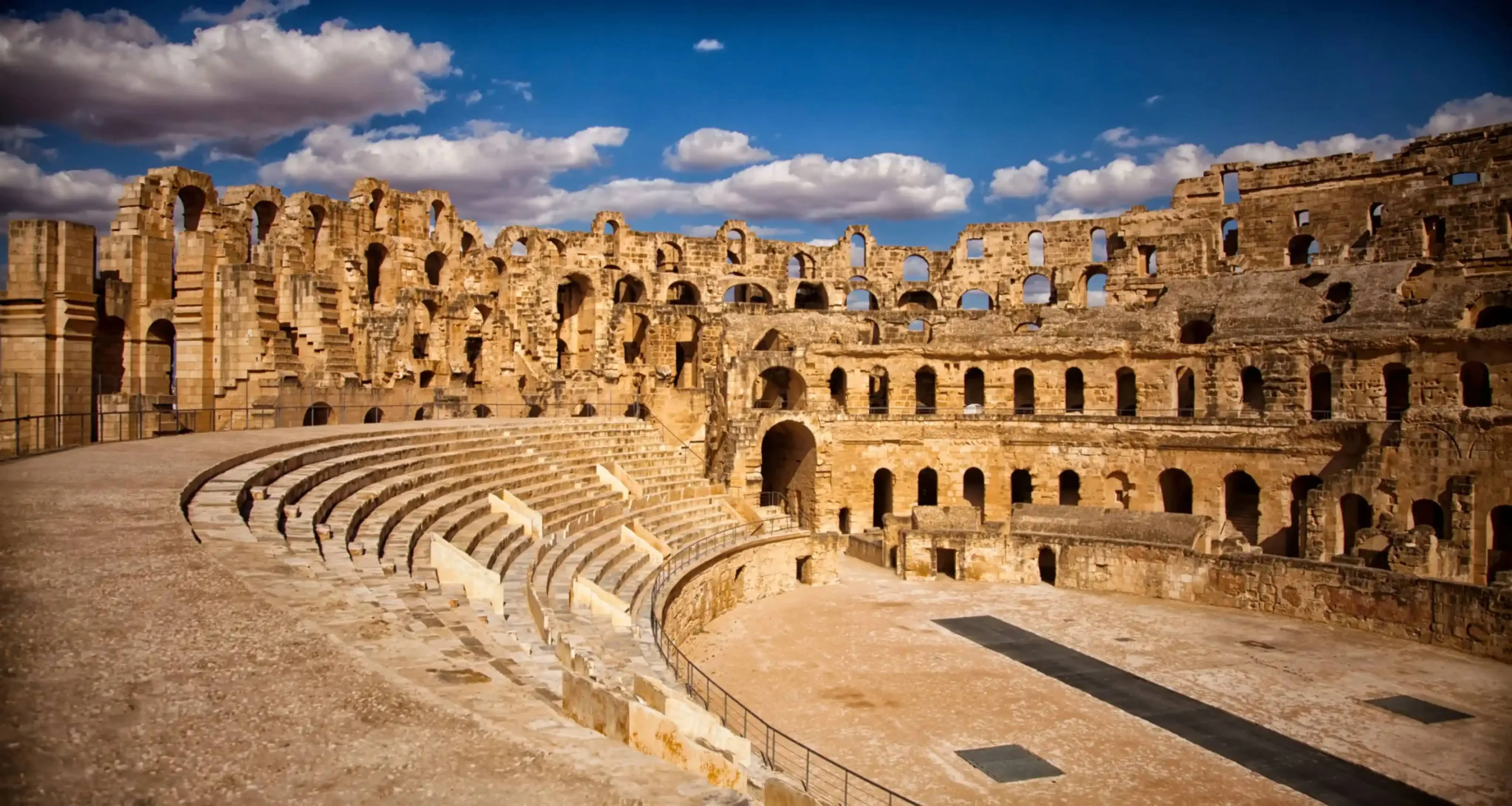 "Ancient Roman amphitheater ruins under a blue sky with scattered clouds."
