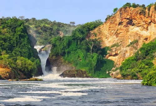Powerful waterfall flowing between lush green cliffs and rocky hills.