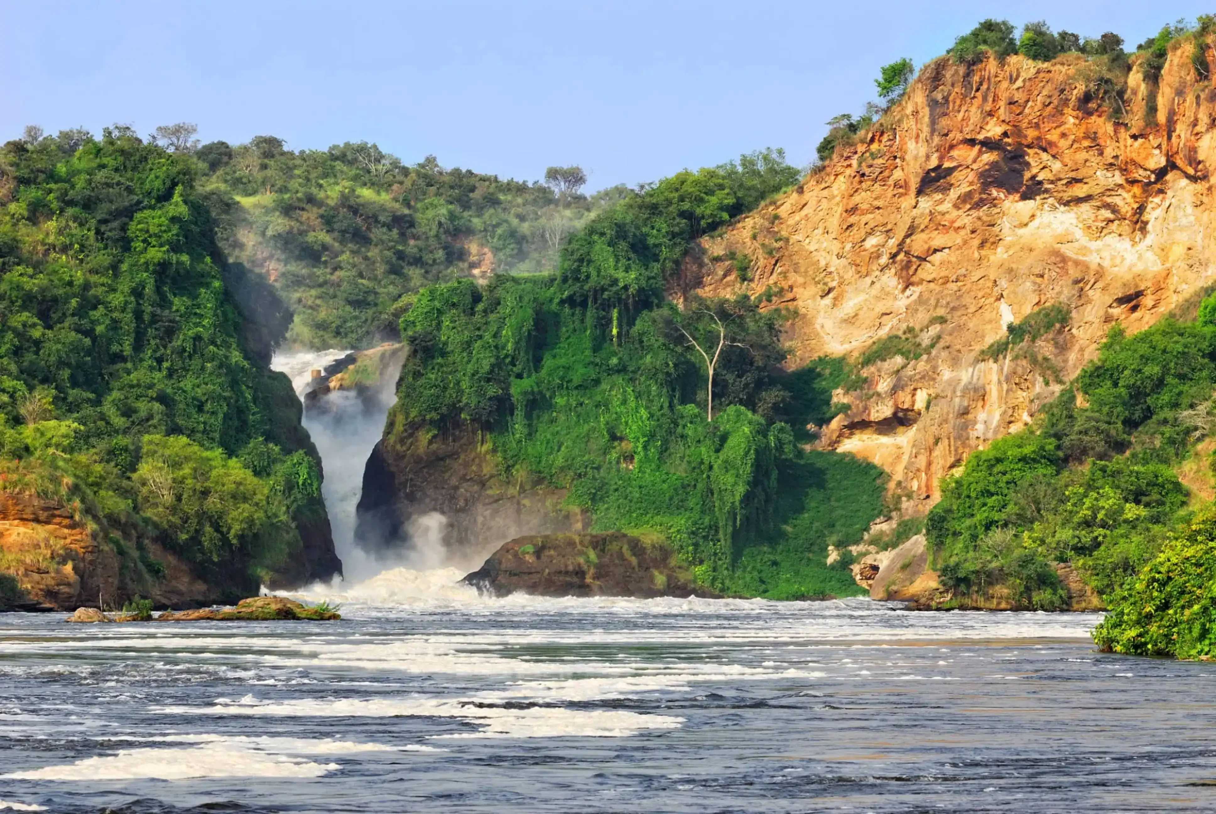 Powerful waterfall flowing between lush green cliffs and rocky hills.