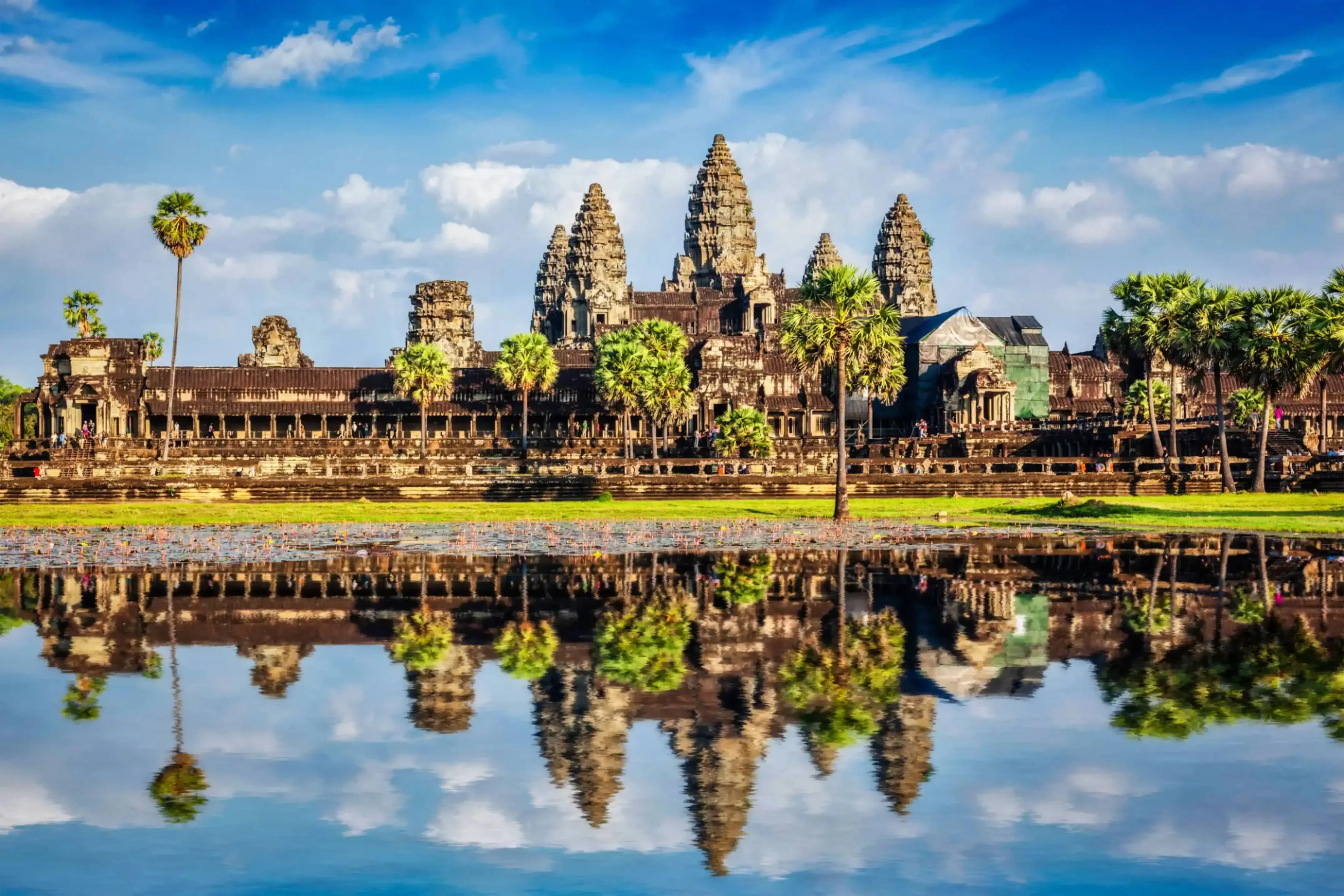 Angkor Wat temple complex reflecting in a tranquil pond under a bright blue sky in Cambodia.