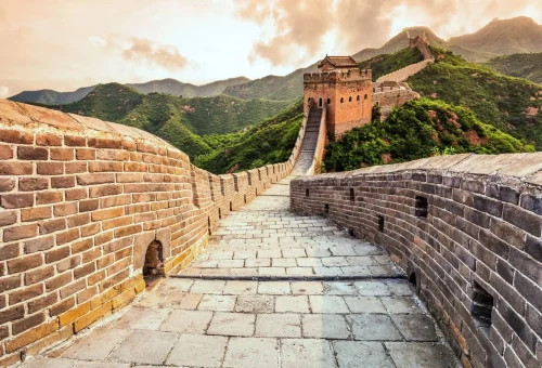 Stone pathway winding along the Great Wall of China with watchtowers and lush green mountains in the background.