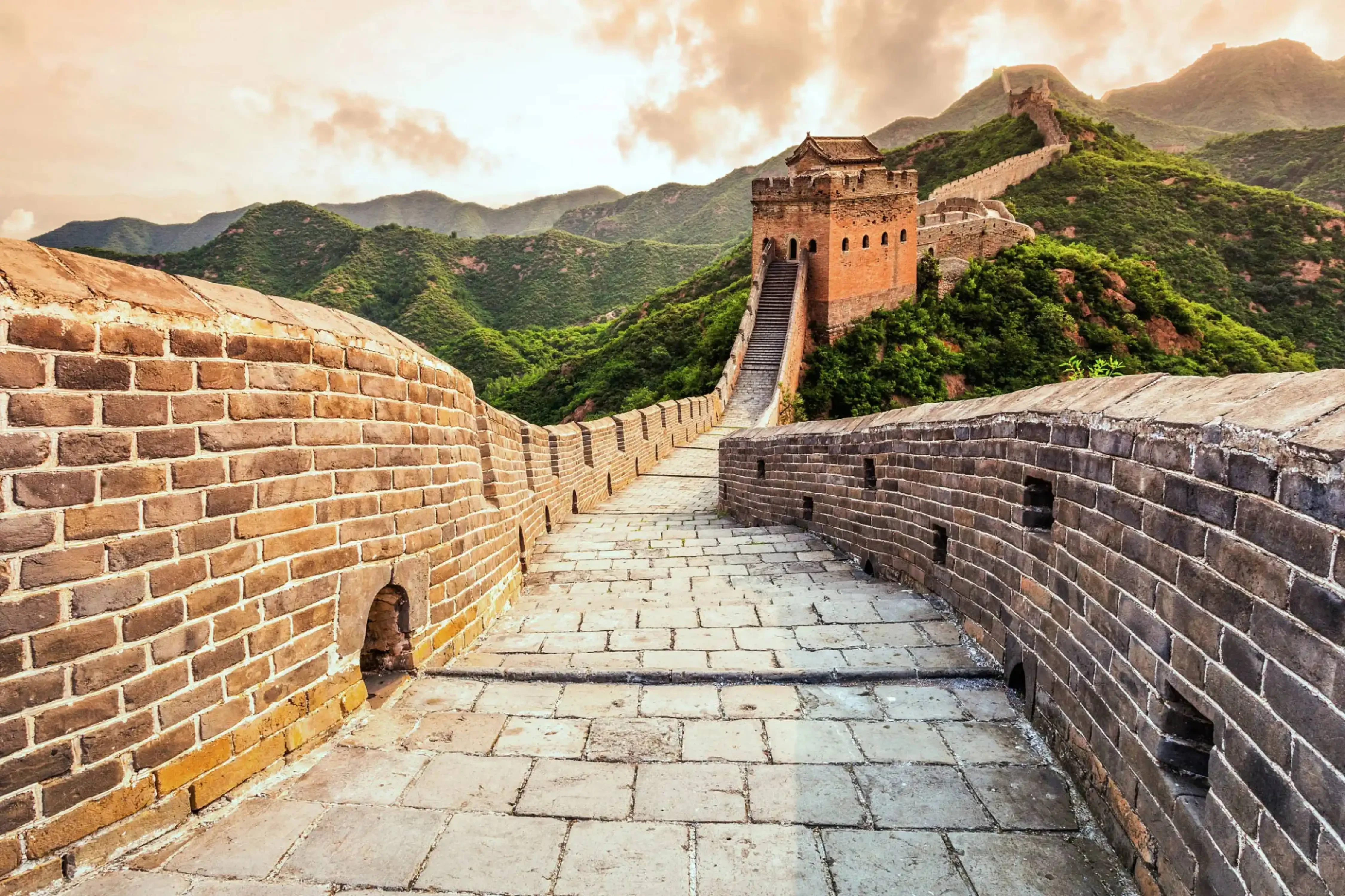 Stone pathway winding along the Great Wall of China with watchtowers and lush green mountains in the background.