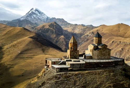 Ancient hilltop monastery surrounded by rugged mountains with a snow-capped peak in the background.