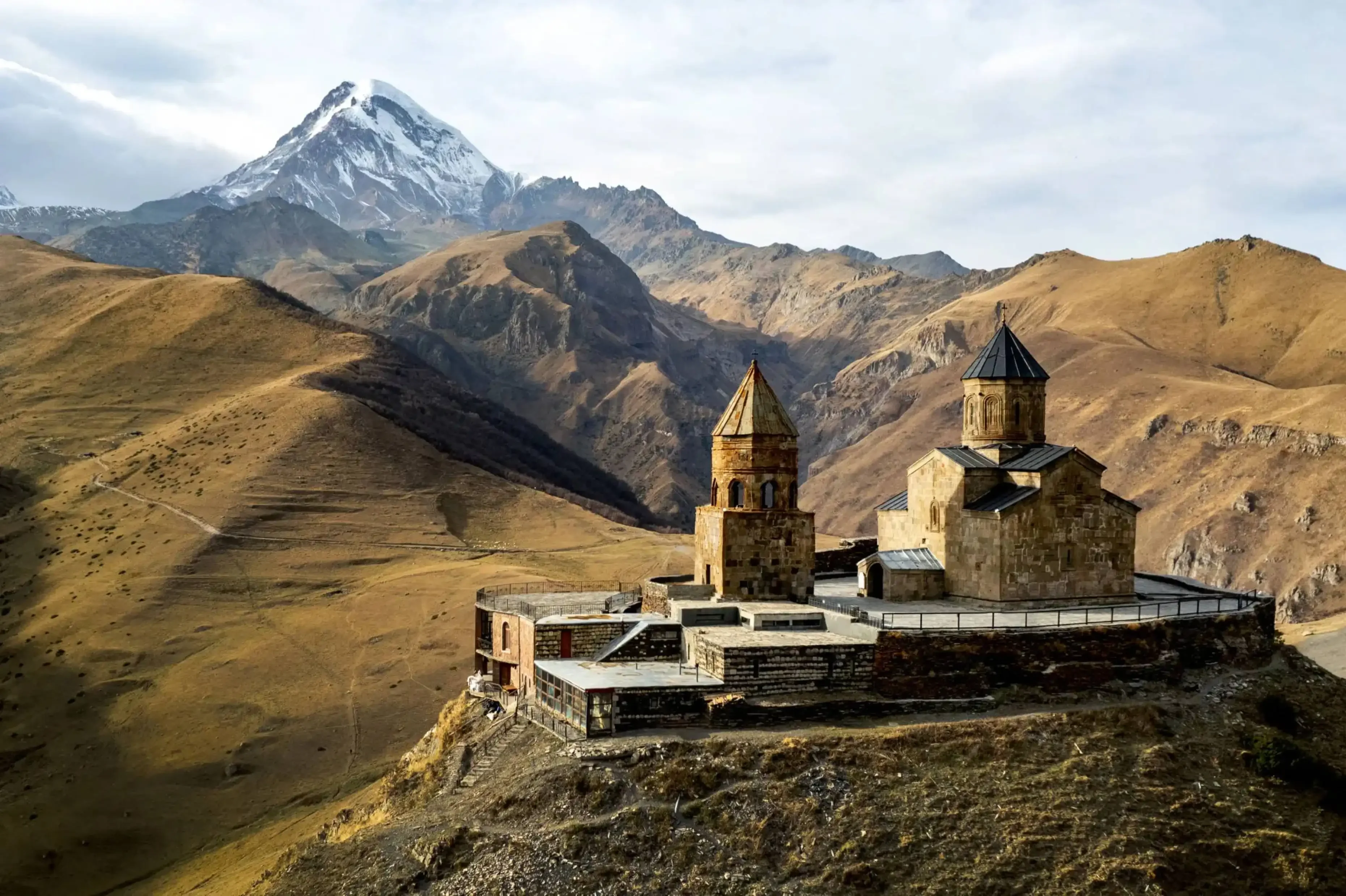 Ancient hilltop monastery surrounded by rugged mountains with a snow-capped peak in the background.