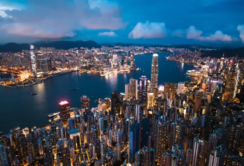 Vibrant cityscape at dusk showcasing a densely packed skyline along a harbor illuminated with sparkling lights.