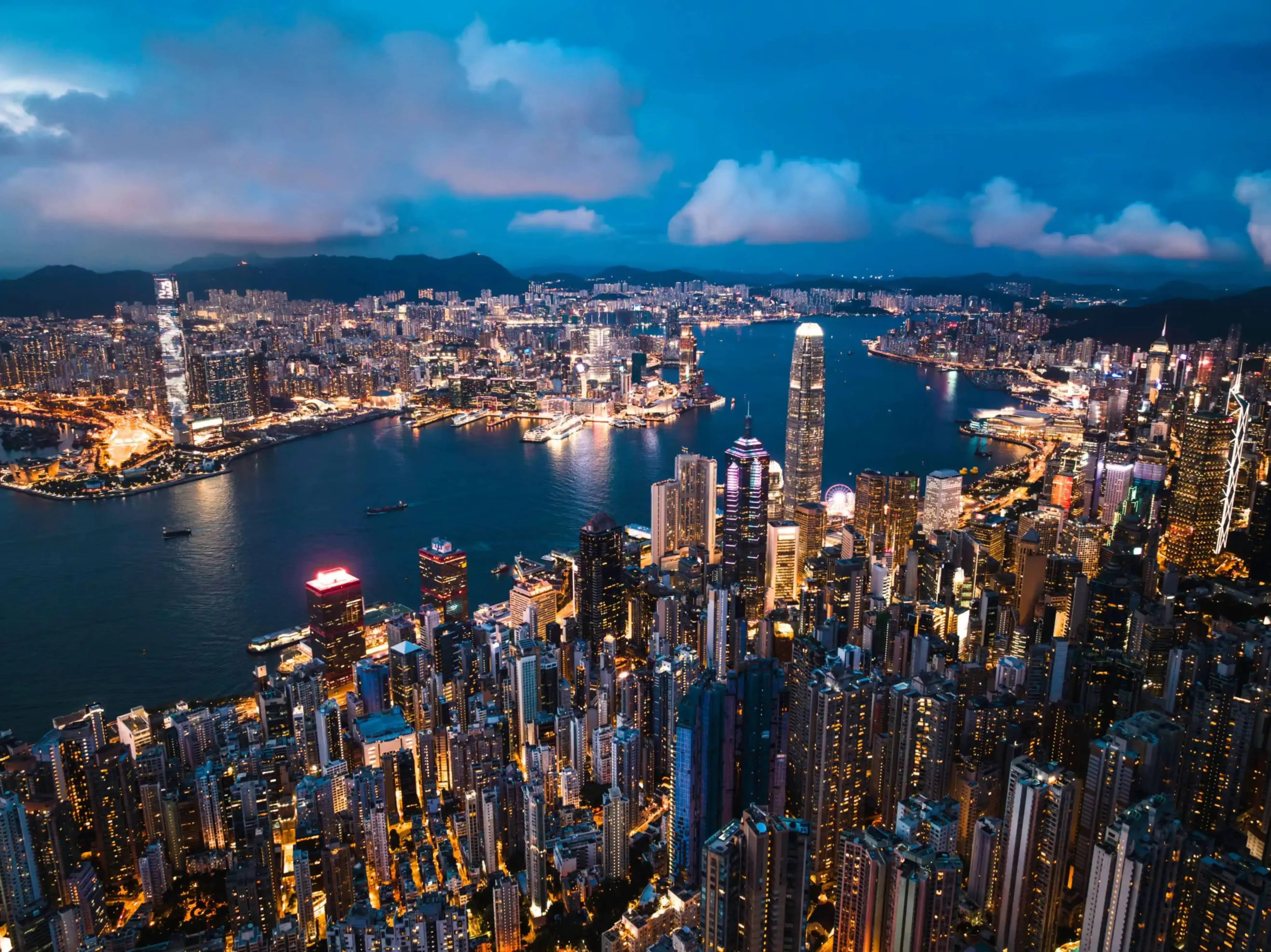 Vibrant cityscape at dusk showcasing a densely packed skyline along a harbor illuminated with sparkling lights.