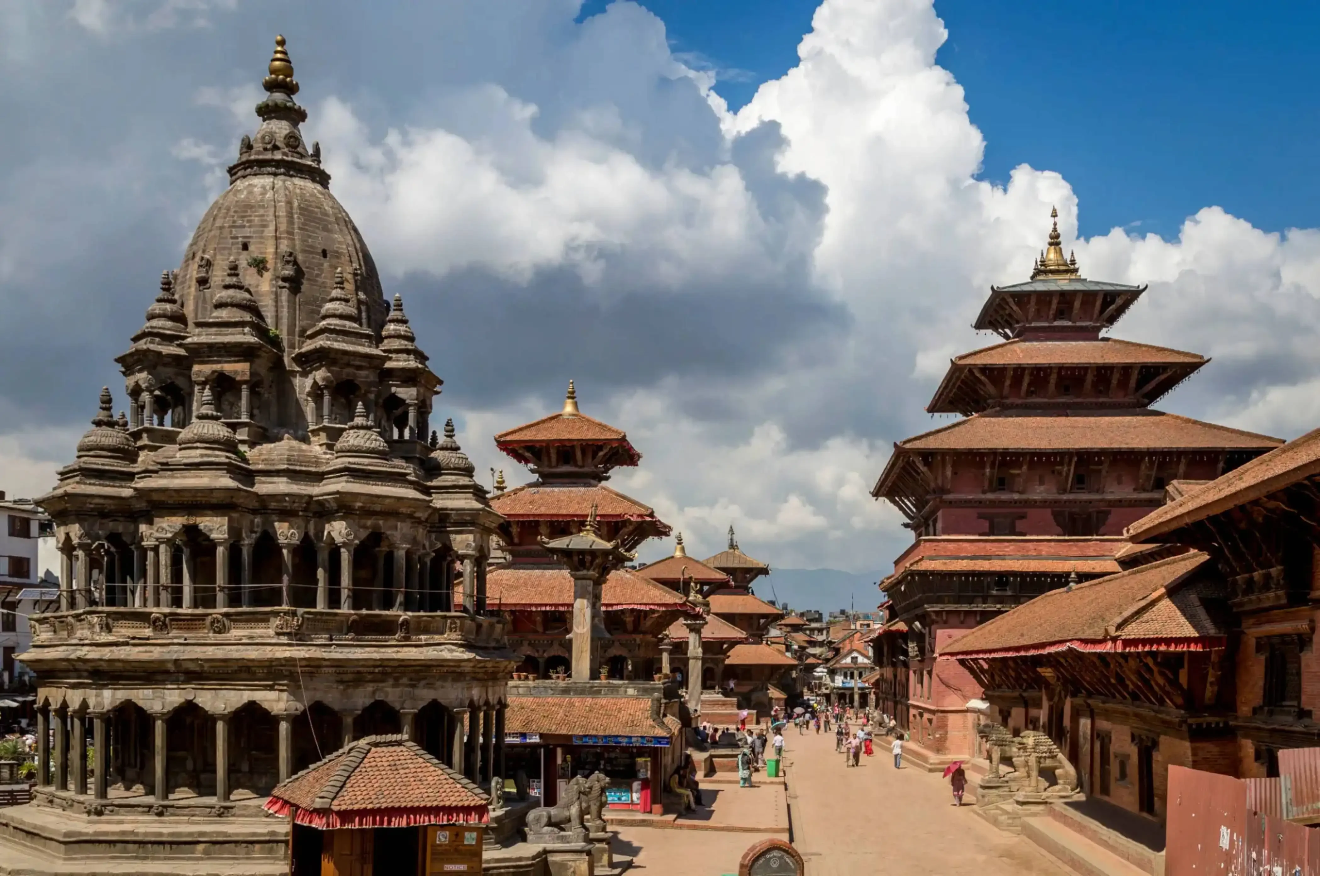 Ancient temples and traditional Newari architecture at Patan Durbar Square in Lalitpur, Nepal, under a dramatic cloudy sky.