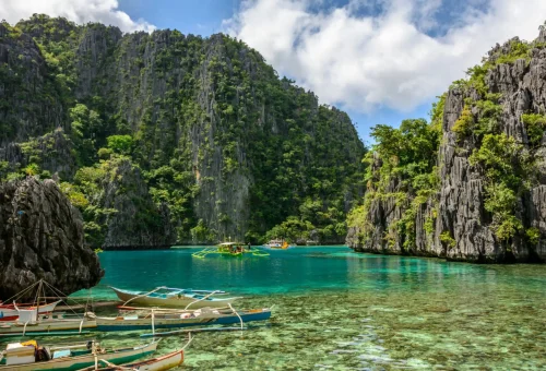 Traditional boats floating on the turquoise waters of a lagoon surrounded by towering limestone cliffs in El Nido, Palawan, Philippines.