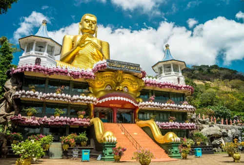 Entrance of the Golden Temple in Dambulla, Sri Lanka, featuring a large seated golden Buddha statue and colorful decorative facade.