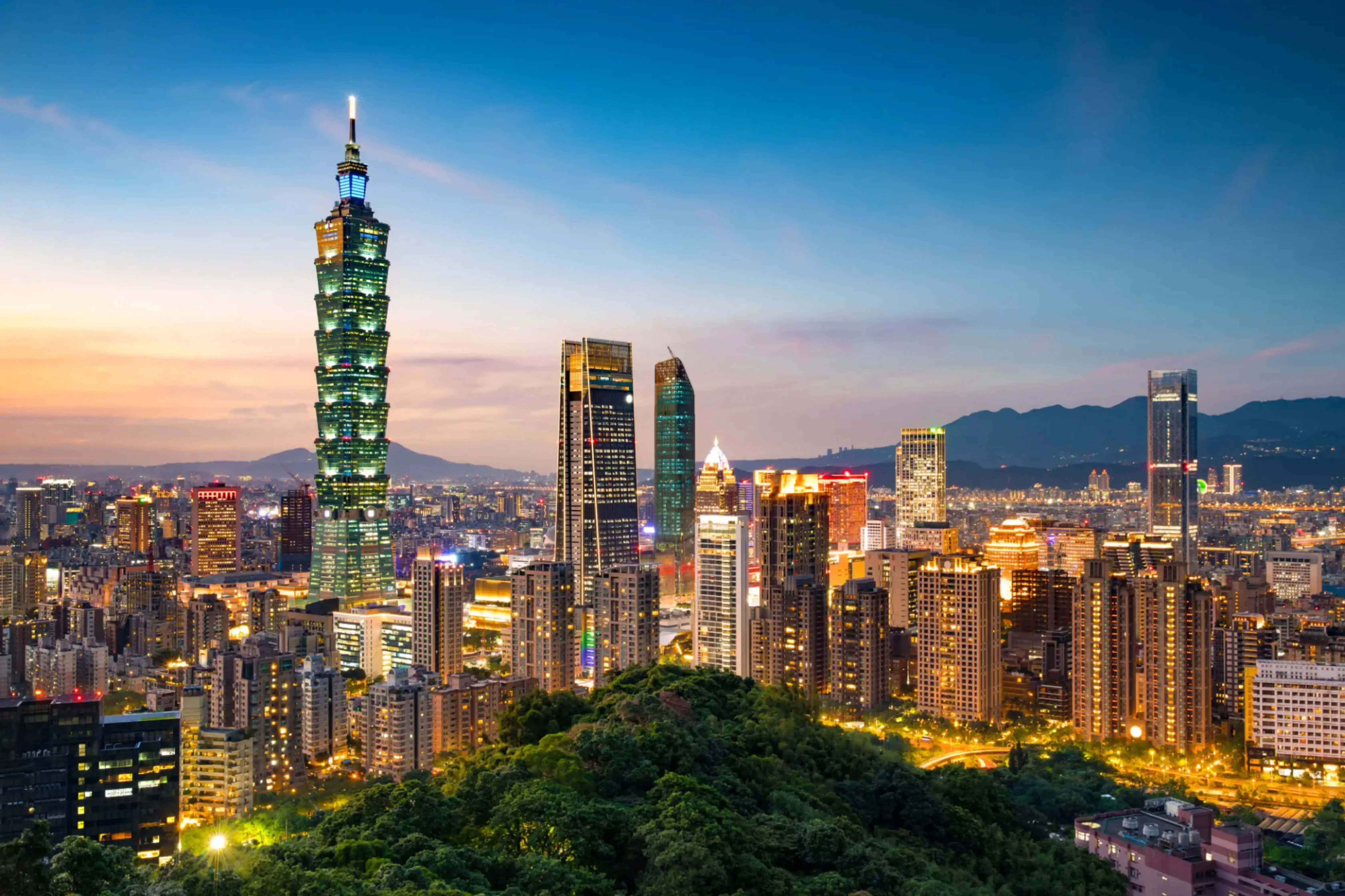 Taipei city skyline at sunset with the iconic Taipei 101 skyscraper prominently visible among surrounding high-rise buildings.