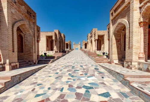 View of the Shah-i-Zinda necropolis in Samarkand, Uzbekistan, featuring a stone mosaic walkway lined with historic mausoleums and intricate Islamic architecture under a clear blue sky.