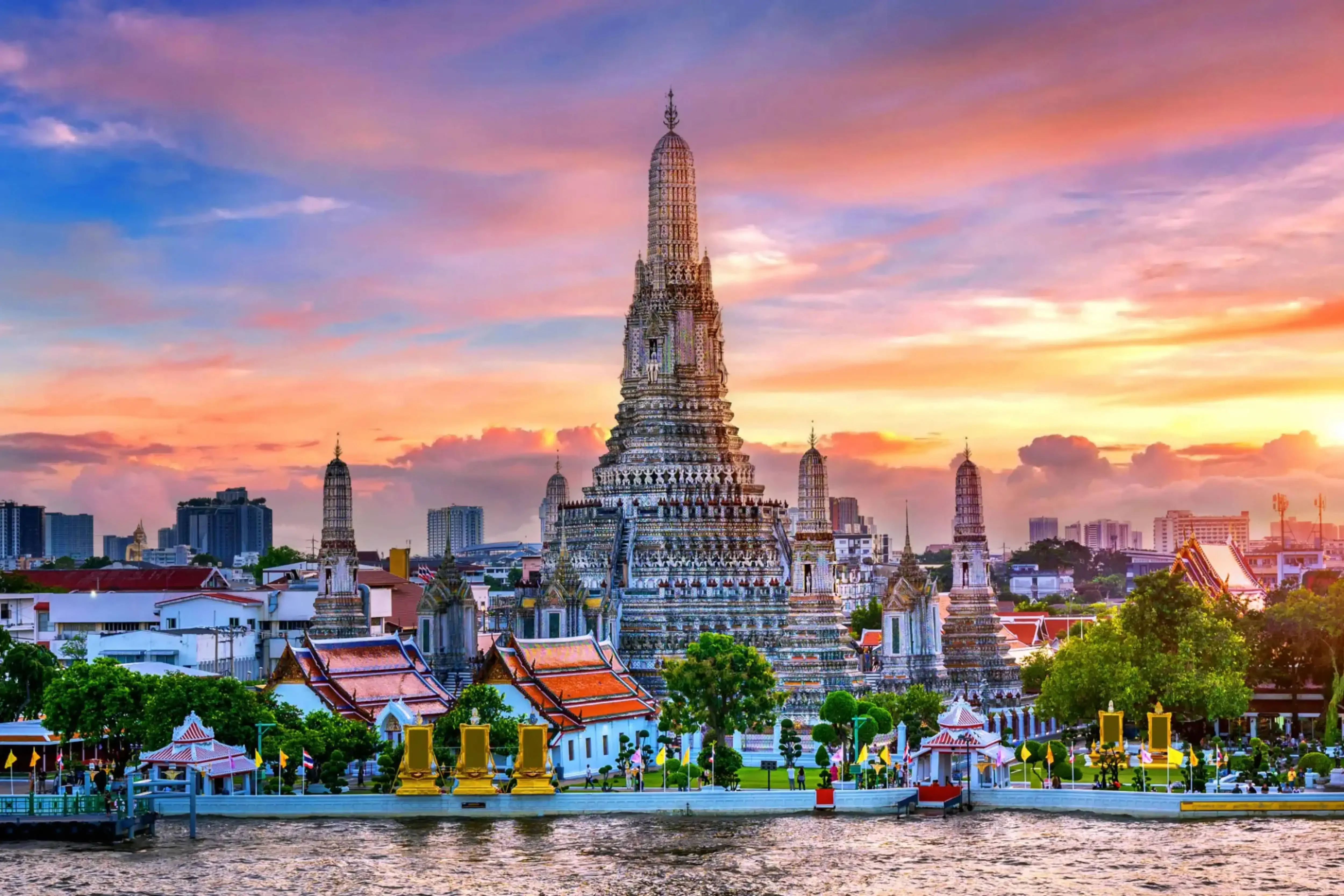 Wat Arun (Temple of Dawn) in Bangkok, Thailand, standing tall on the west bank of the Chao Phraya River with intricate spires and a glowing sunset sky in the background.