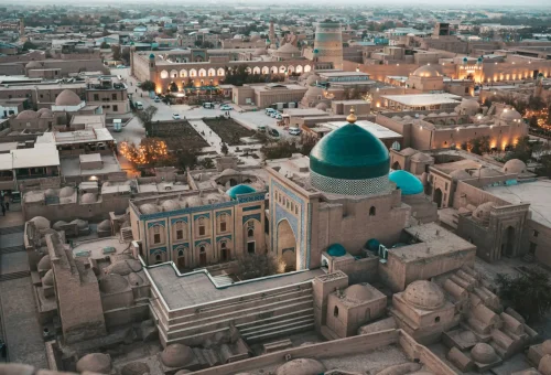 Aerial view of the historic city of Khiva, Uzbekistan, showcasing its mud-brick architecture, turquoise-domed mosques, and ancient minarets at dusk.