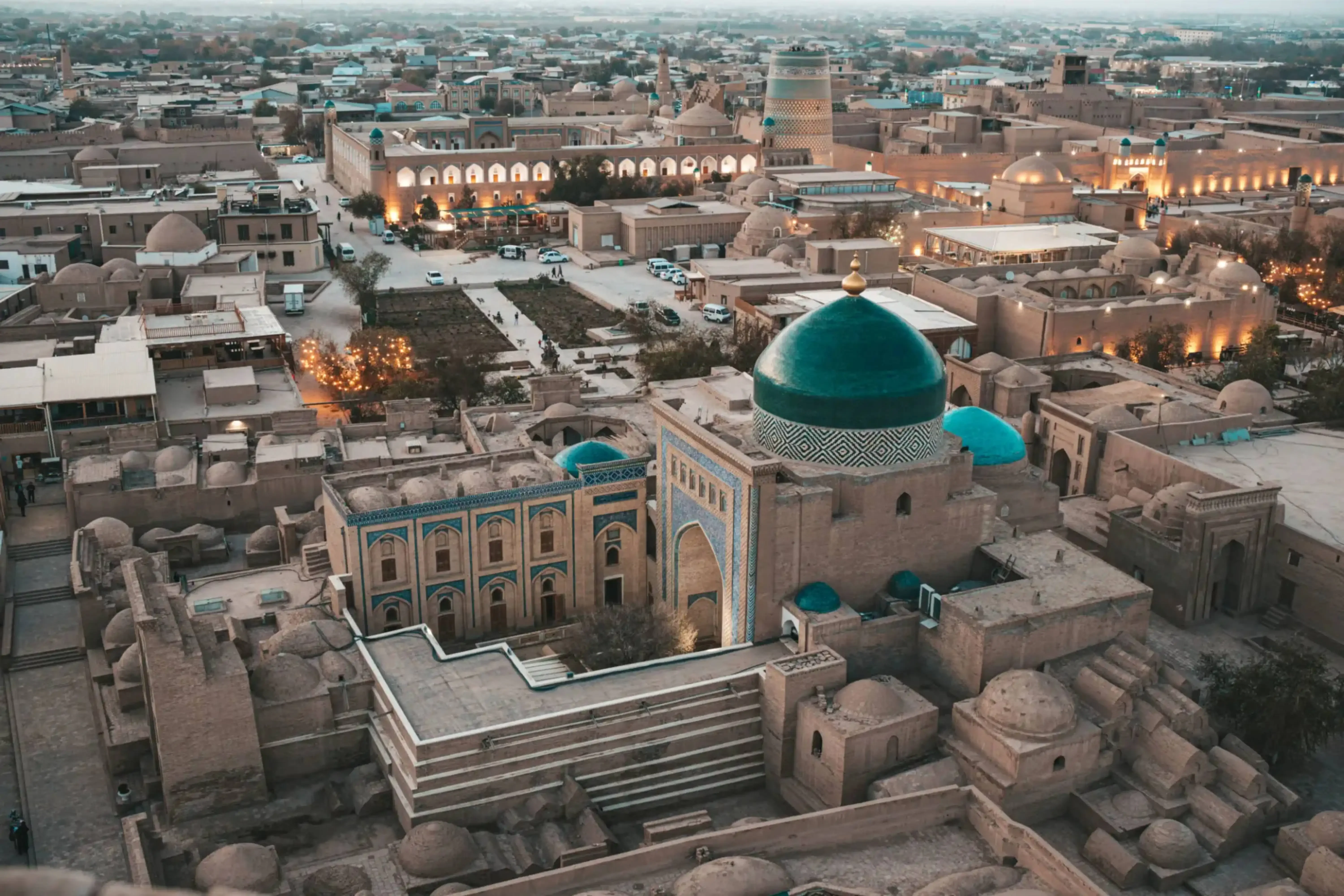 Aerial view of the historic city of Khiva, Uzbekistan, showcasing its mud-brick architecture, turquoise-domed mosques, and ancient minarets at dusk.