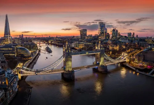 Sunset view over London with Tower Bridge illuminated and the Shard skyscraper in the background, reflecting on the River Thames.