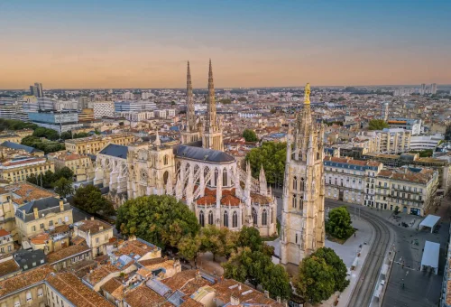 Aerial view of Bordeaux Cathedral (Saint-André) in Bordeaux, France, with twin spires rising above the city’s terracotta rooftops and historic architecture during sunset.