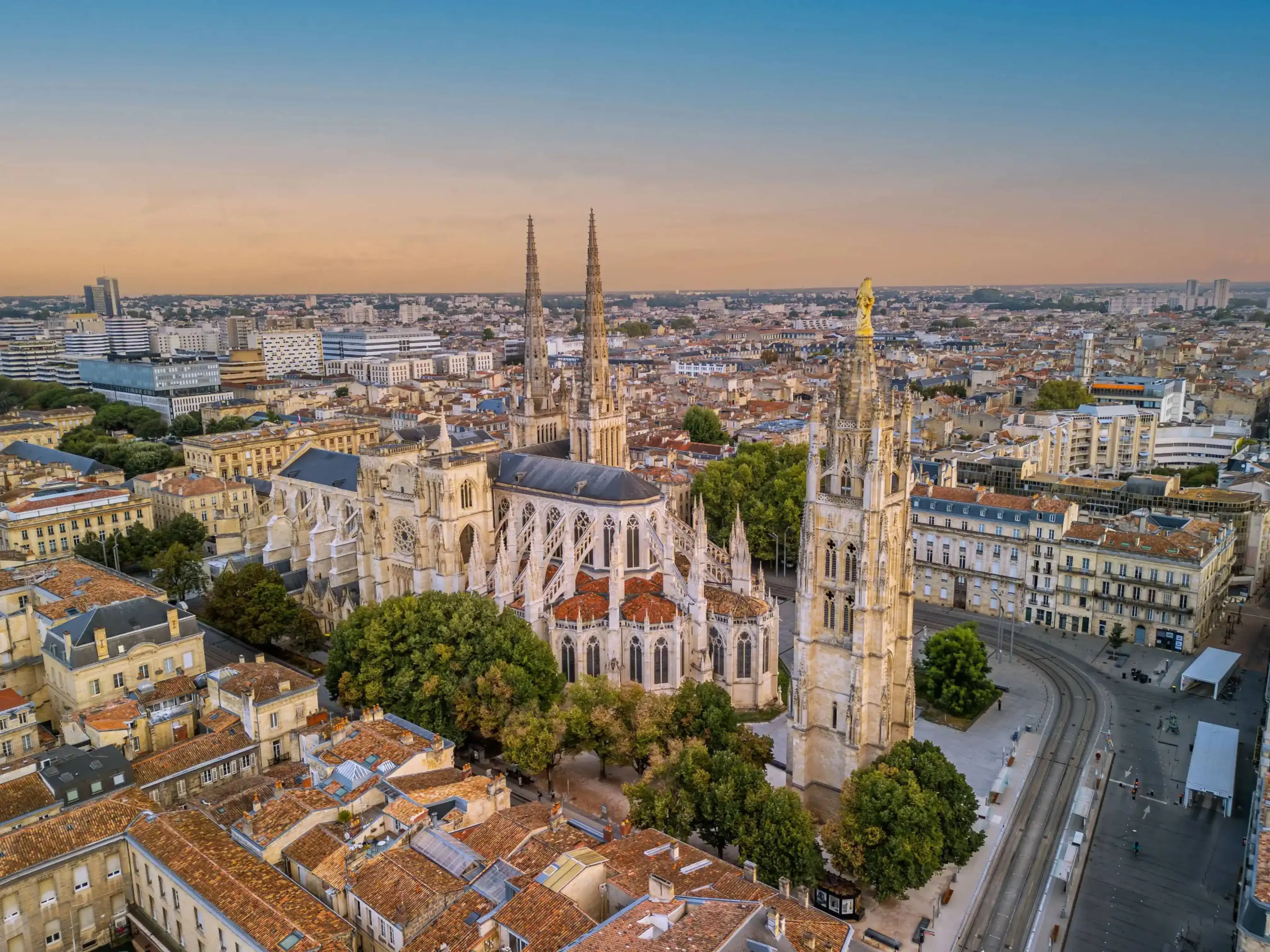 Aerial view of Bordeaux Cathedral (Saint-André) in Bordeaux, France, with twin spires rising above the city’s terracotta rooftops and historic architecture during sunset.