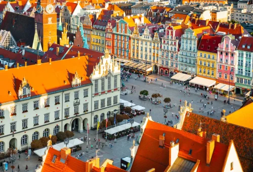 Aerial view of Wrocław Market Square in Poland, featuring colorful historic buildings, red-tiled roofs, and people walking in the vibrant city plaza.