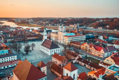 Aerial view of the historic Old Town of Grodno, Belarus, featuring the Jesuit Cathedral (St. Francis Xavier Cathedral) and red-roofed buildings near the Neman River during sunset.