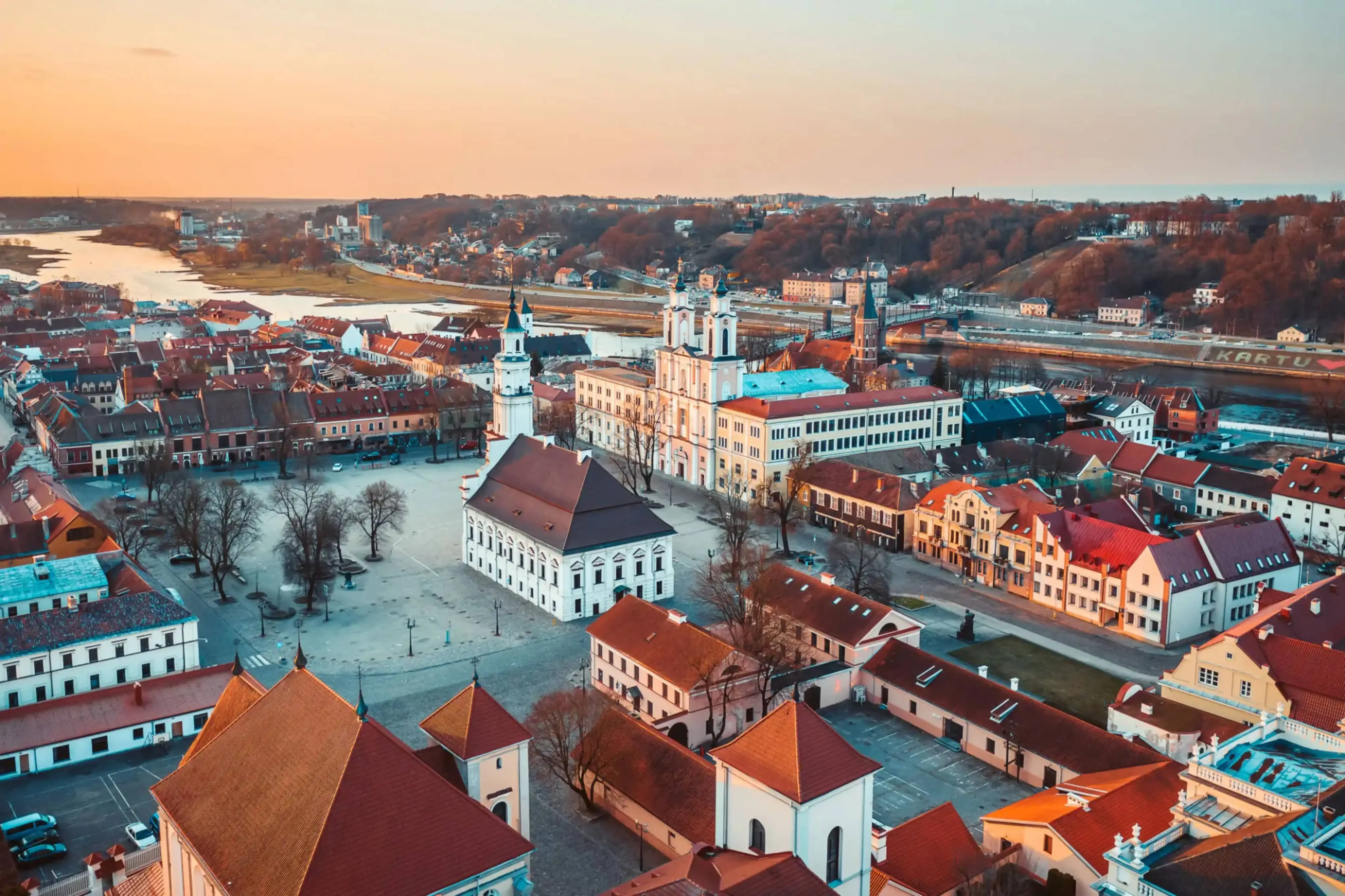 Aerial view of the historic Old Town of Grodno, Belarus, featuring the Jesuit Cathedral (St. Francis Xavier Cathedral) and red-roofed buildings near the Neman River during sunset.